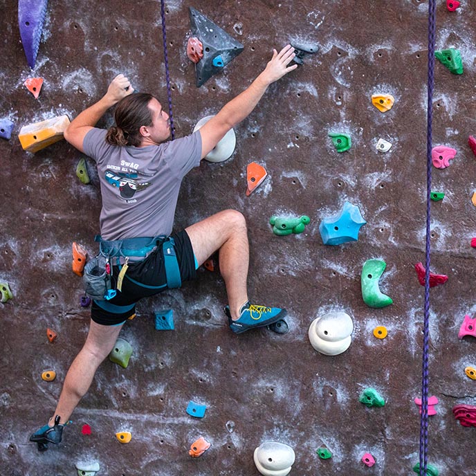 Climber reaching for a handhold on an indoor climbing wall.