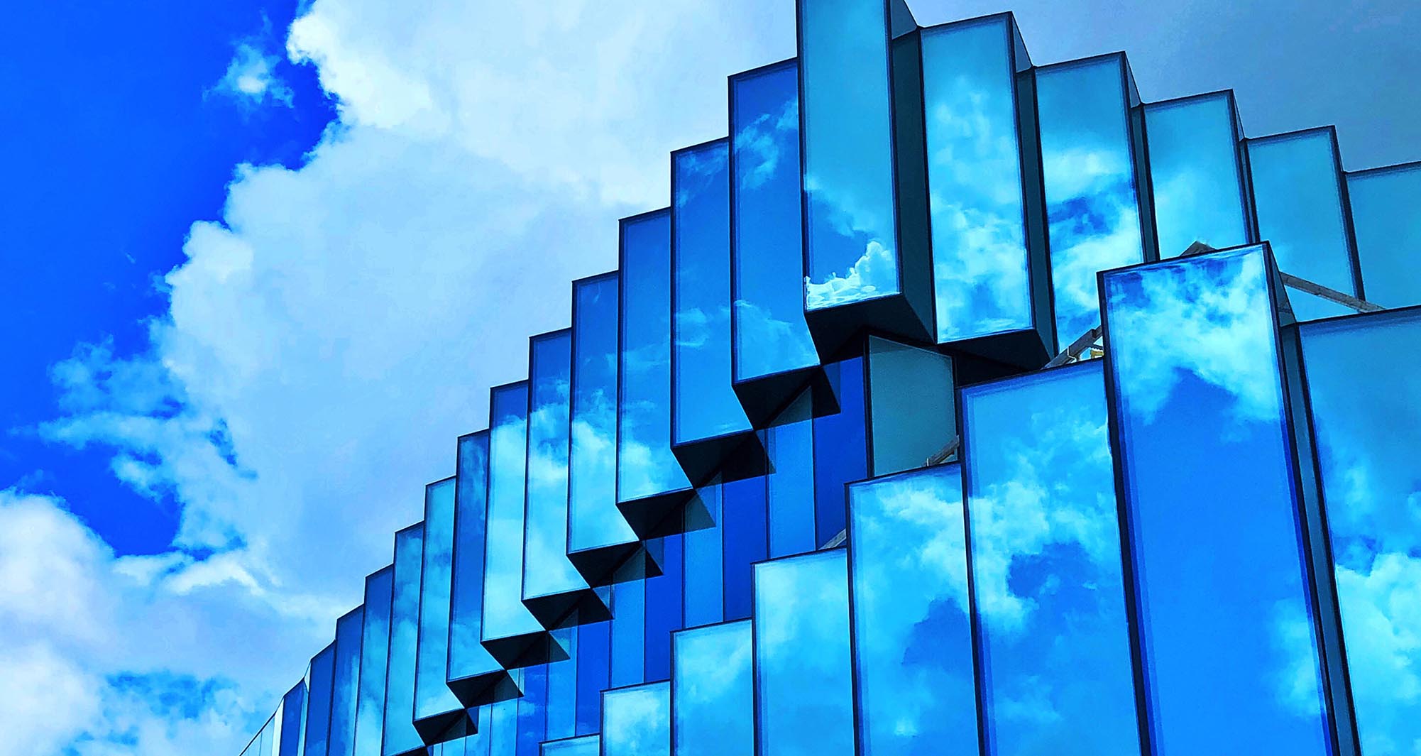 Closeup of the Student Innovation Center with blue skies and clouds reflecting off the windows.