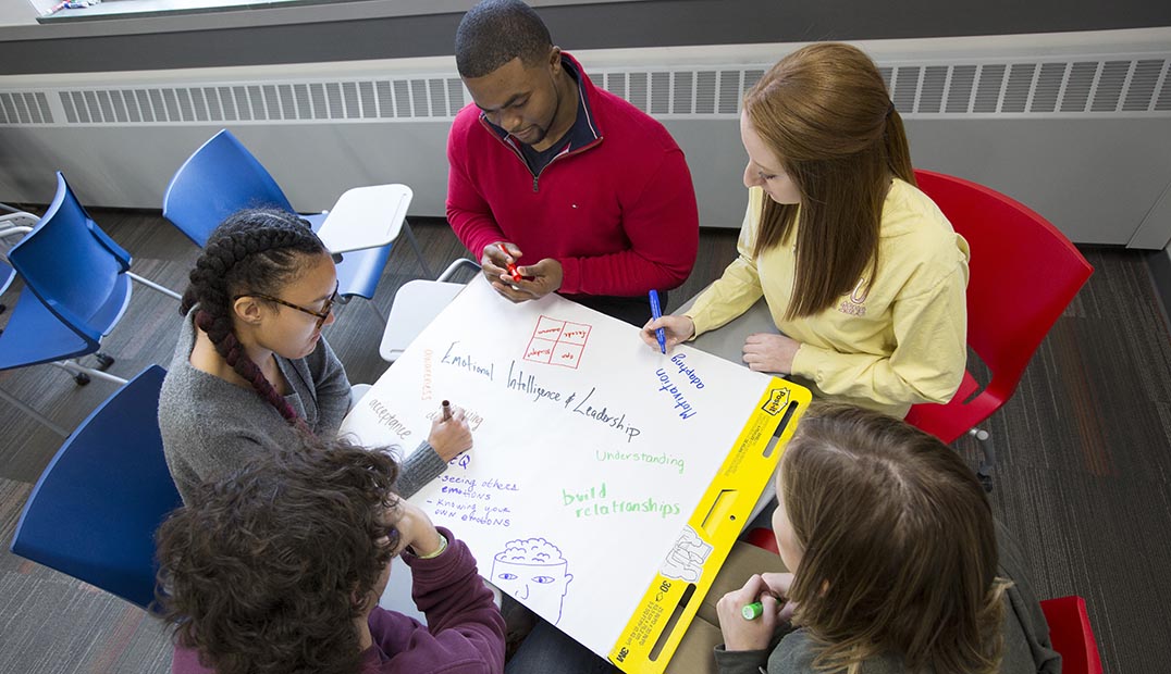 Five students work on a project while seated at a table.